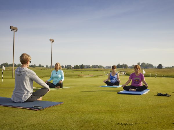 a group of people sitting on mats in a grassy field